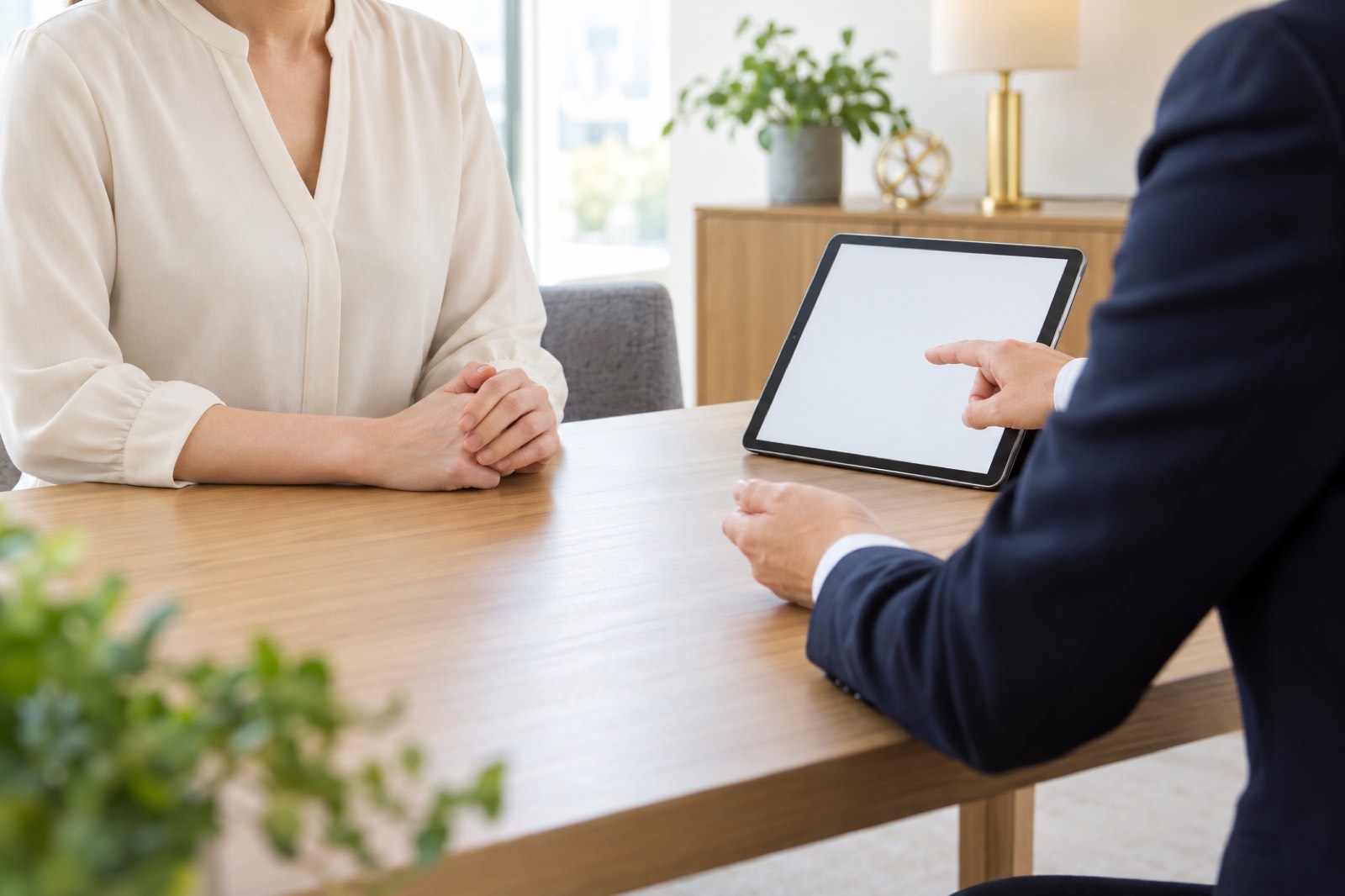 明るい相談室で、紺のジャケットのカウンセラーがタブレットを示しながら、手を重ねて座る女性と話している様子