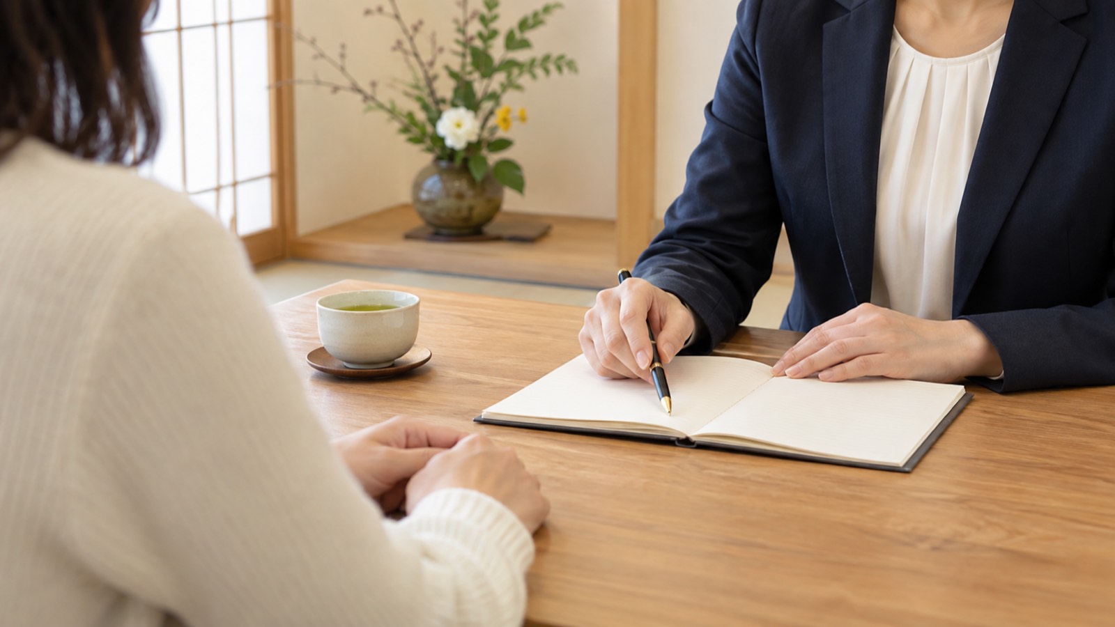 落ち着いた部屋で、ノートを前に相談するカウンセラーと相談者の手元