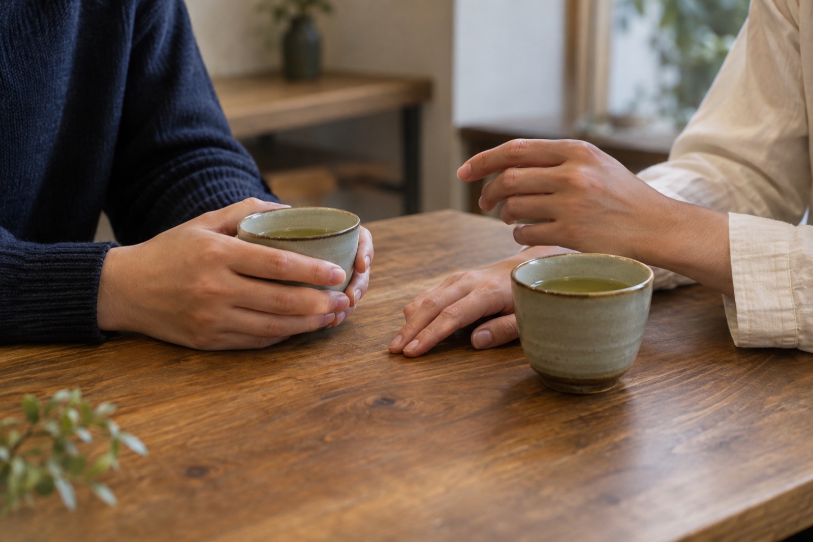 木のテーブルで湯のみを前に、向き合って話す二人の手元