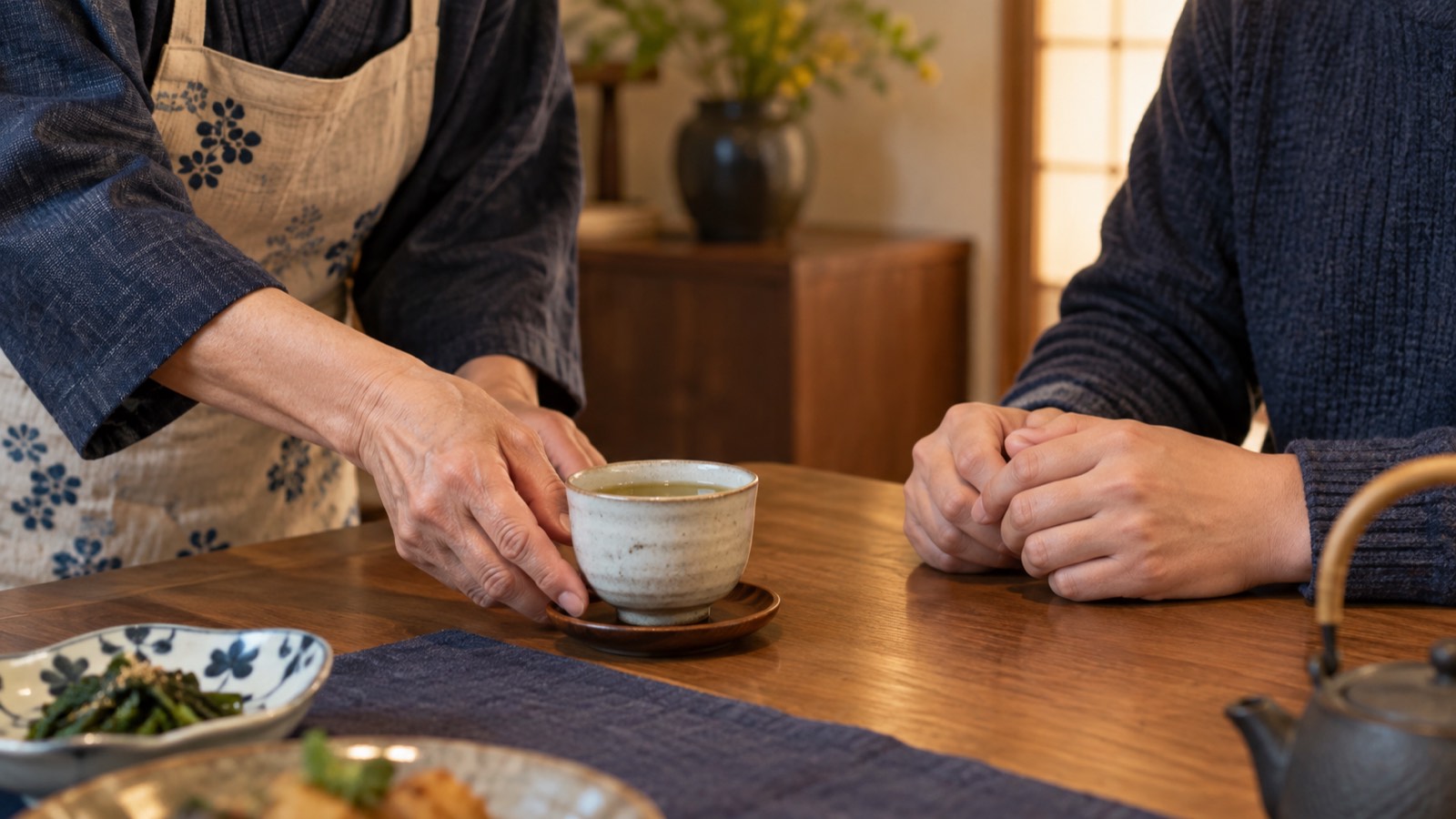 食卓で、親が大人の子の前にそっとお茶を置く手元