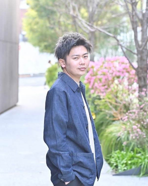 花の咲く小道で振り返り、カメラに向かってほほえむデニムジャケットの男性