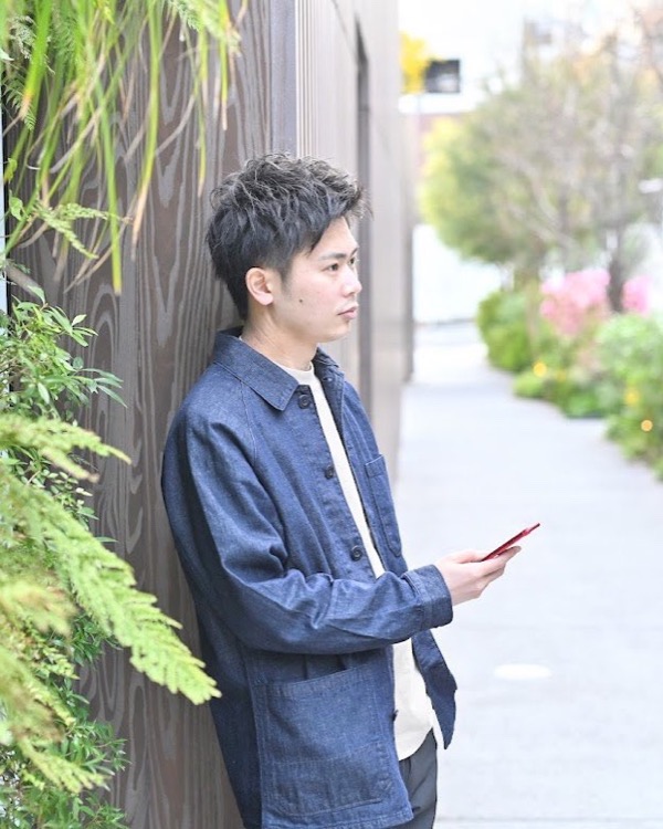 緑の壁にもたれてスマホを見る男性の横顔